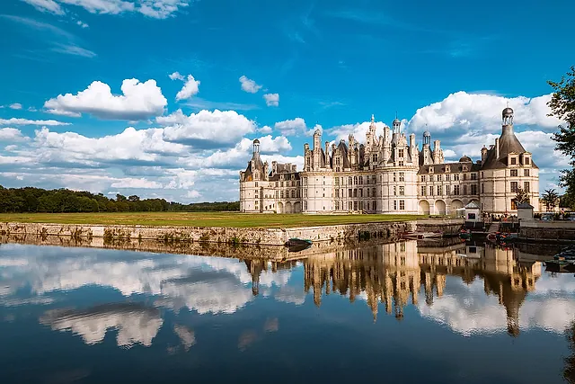 Château de Chambord mirrored in the water of its canal under a sky of white clouds