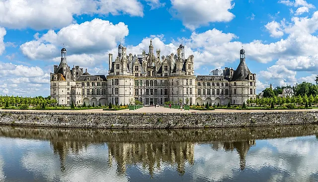 The north-west facade of Château de Chambord reflected in the canal under a blue sky